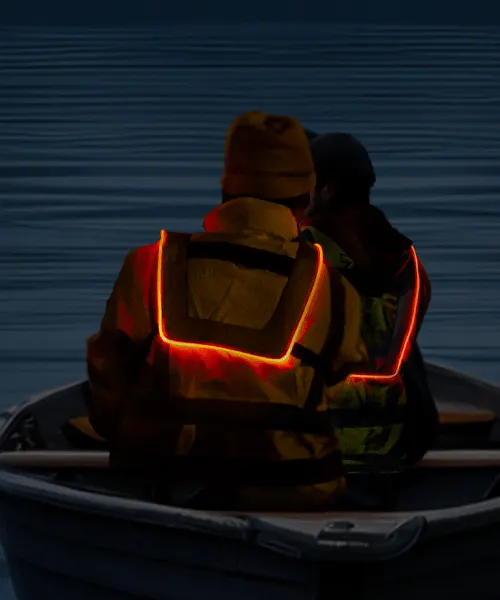 Dos pescadores, de espaldas en un bote, iluminados por la potente luz del chaleco Heavy Duty, destacando en la oscuridad