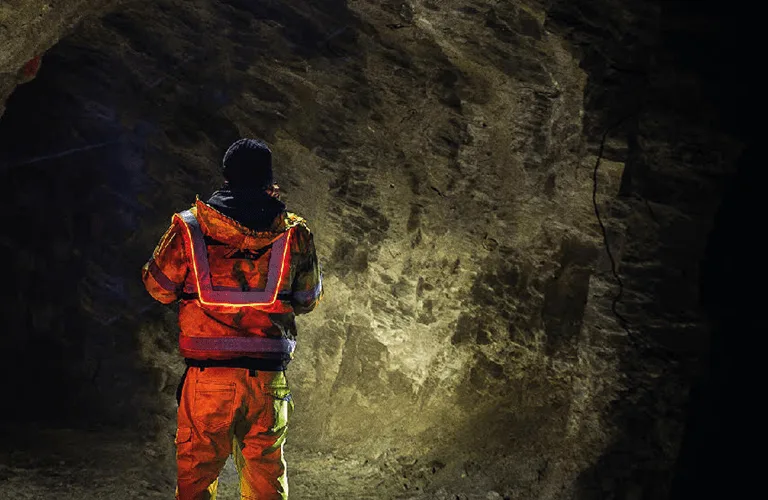 Trabajador minero ingresando a un túnel, con su chaleco Heavy Duty activado, proporcionando iluminación adicional en el oscuro ambiente subterráneo