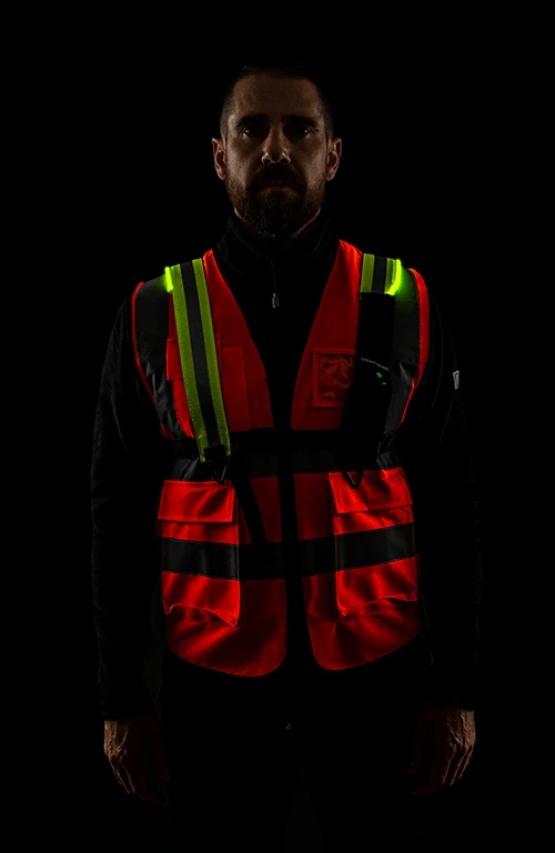 Modelo posando frente a un fondo oscuro de estudio, usando un chaleco de geólogo y encima, un chaleco Heavy Duty de EquiRay en color amarillo, activado para resaltar en la oscuridad